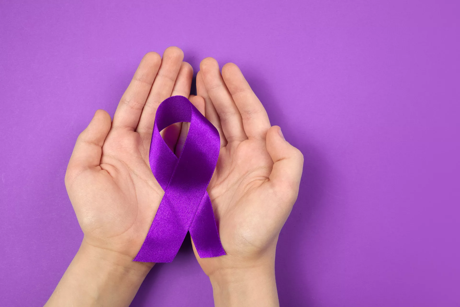 Hands holding purple ribbon on purple background